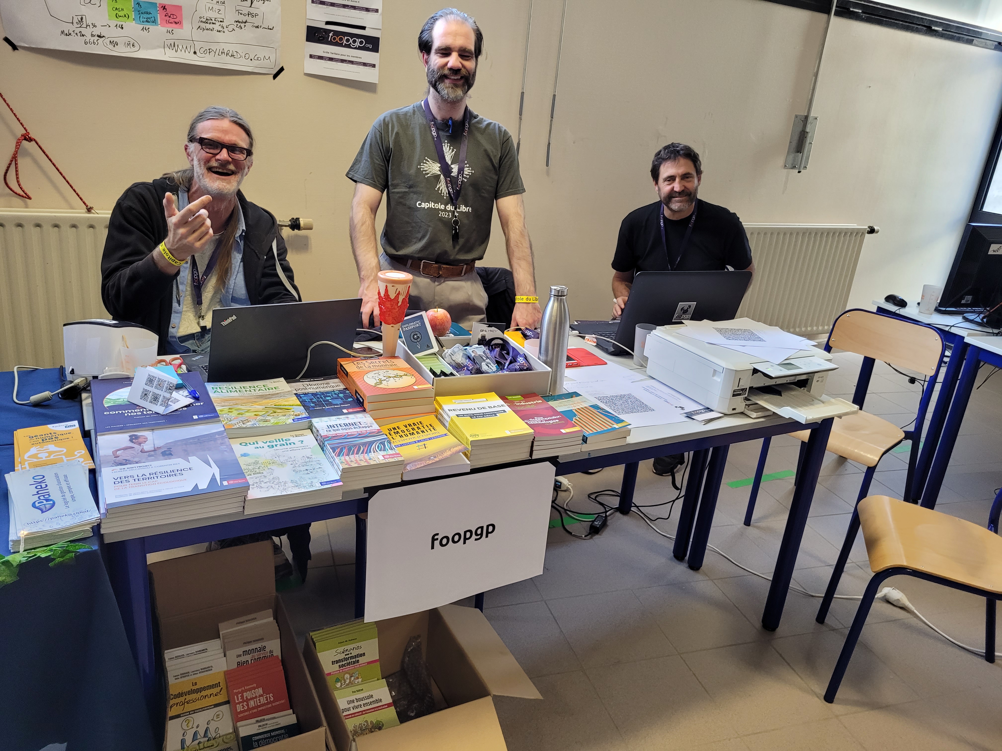 3 smiling foopgp members behind the association&rsquo;s stand at the capitole du libre (2024-11-16 Toulouse)